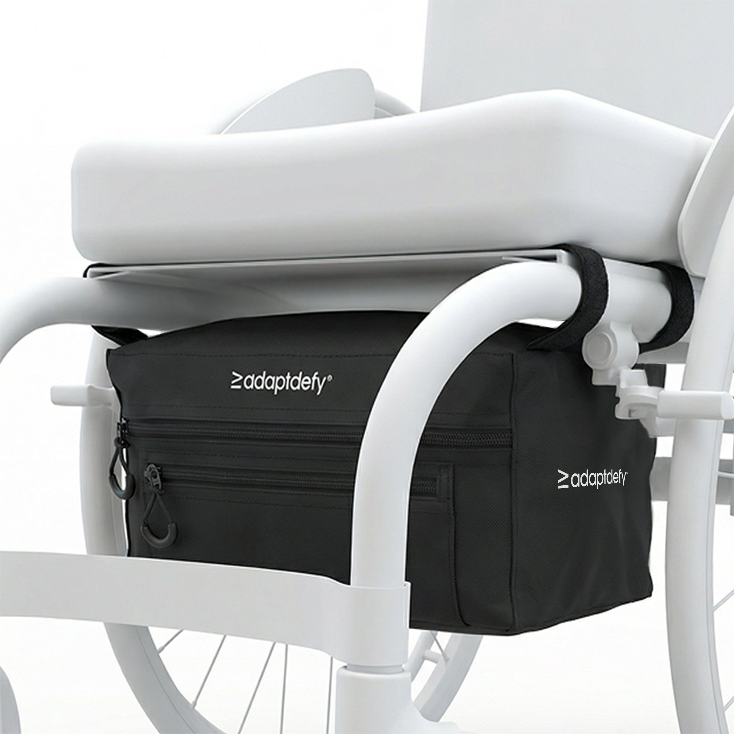 Black bag attached to a wheelchair via velcro straps with 'adaptdefy' branding. The bag is installed under the seat and has a main pocket and a smaller front pocket, both have zips with finger loops.