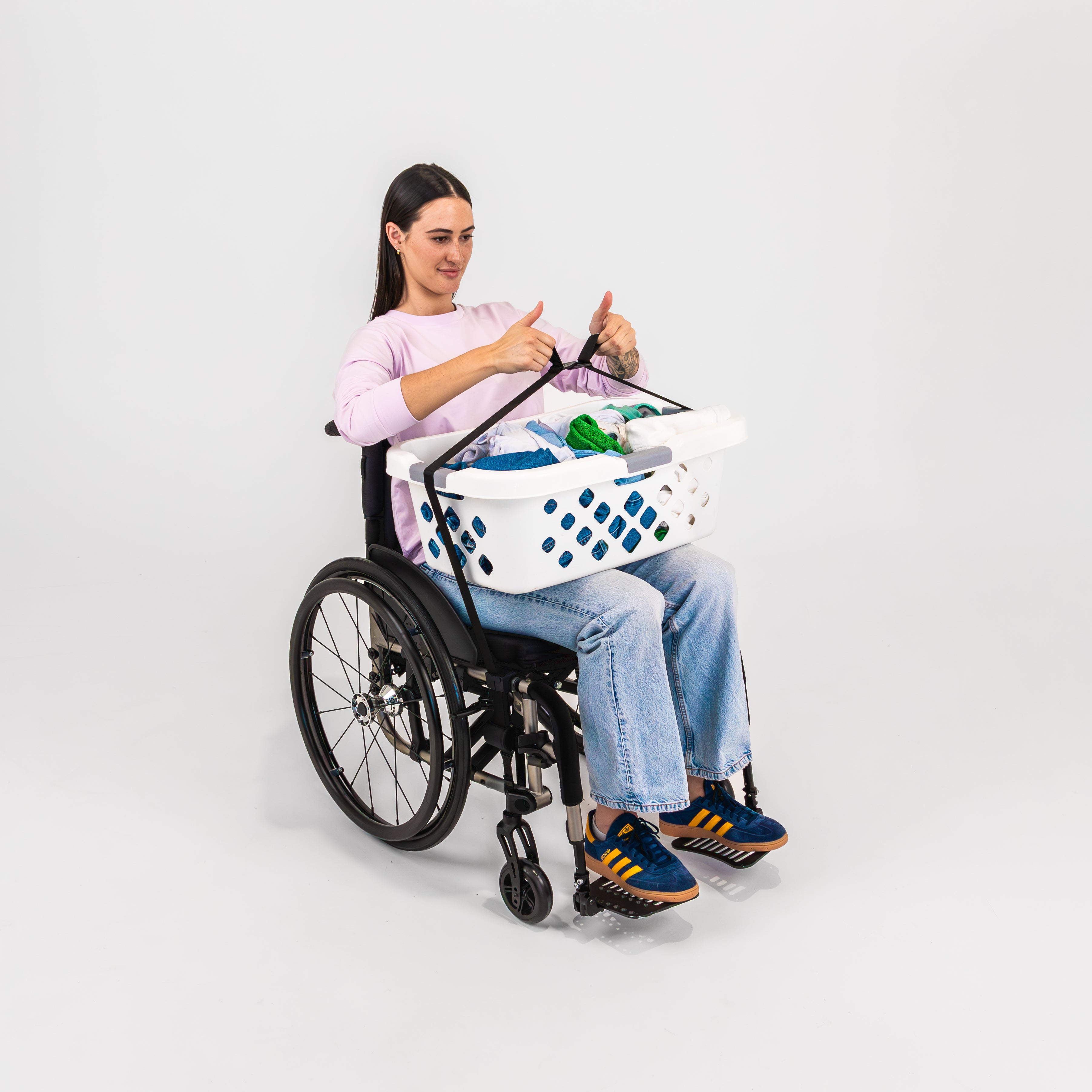 Smiling women with pink t-shirt seated in a wheelchair clipping buckles over a washing basket to her lap using LapStacker Flex.