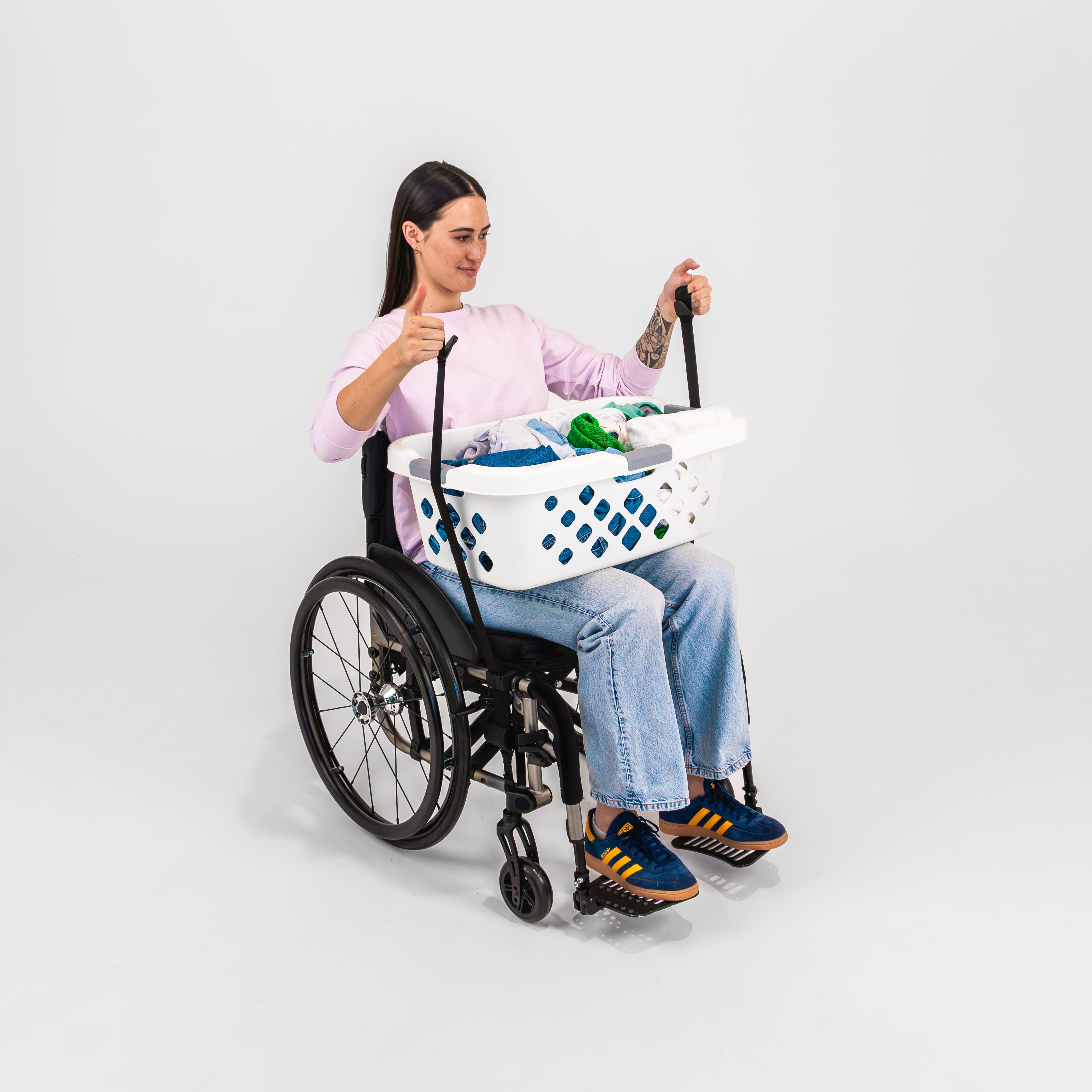 Smiling women with pink t-shirt seated in a wheelchair pulling straps up over a washing basket to her lap using LapStacker Flex.