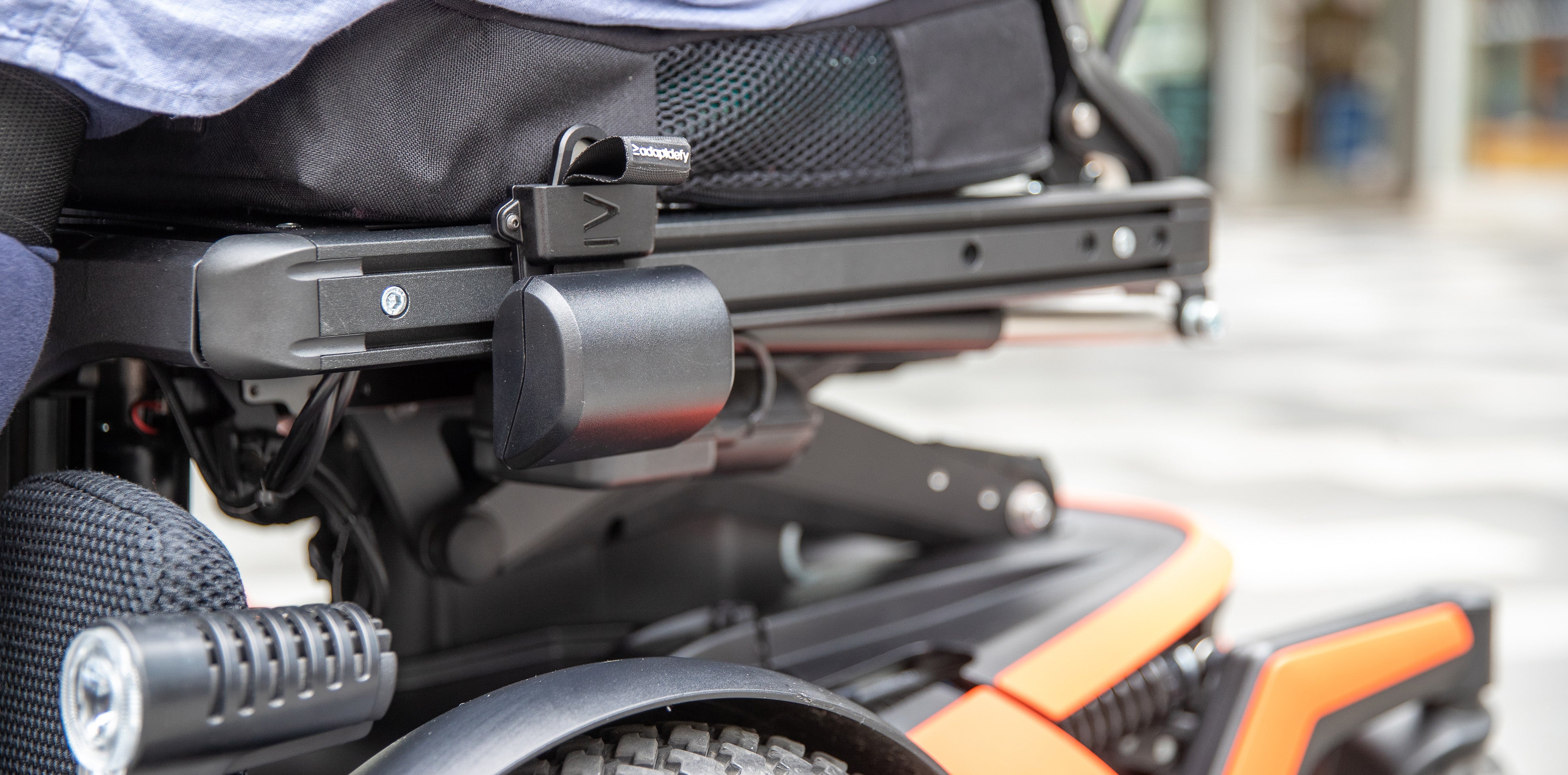 Closeup of LapStacker XD installed on the side of a power wheelchair, showing a black retractor unit on the t track