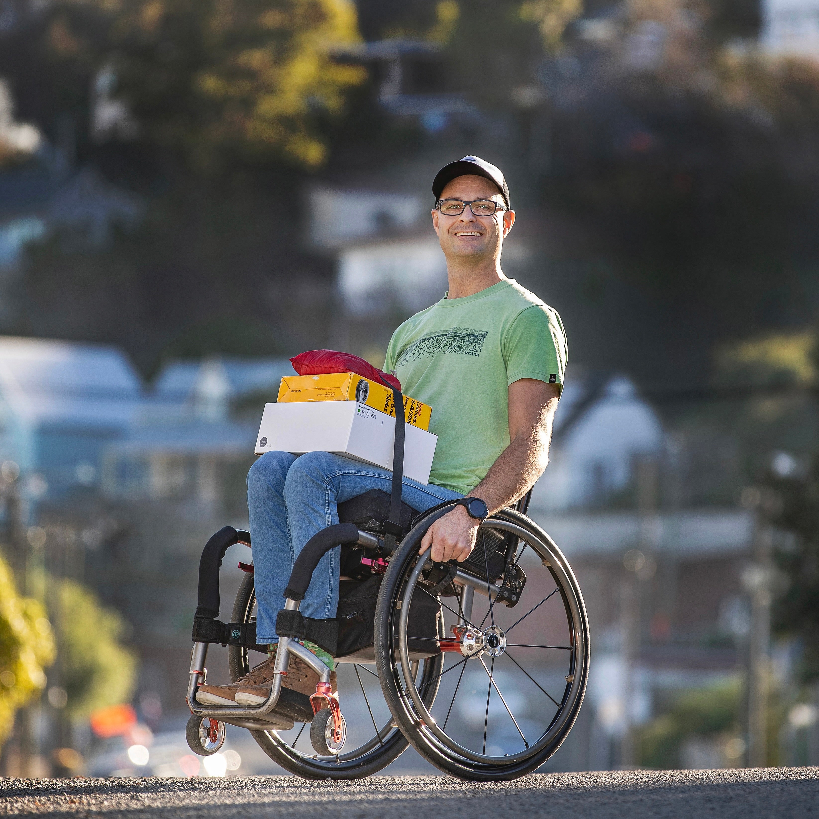 Man in a wheelchair smiling and doing a wheelie, with boxes on his lap, secured with a LapStacker.