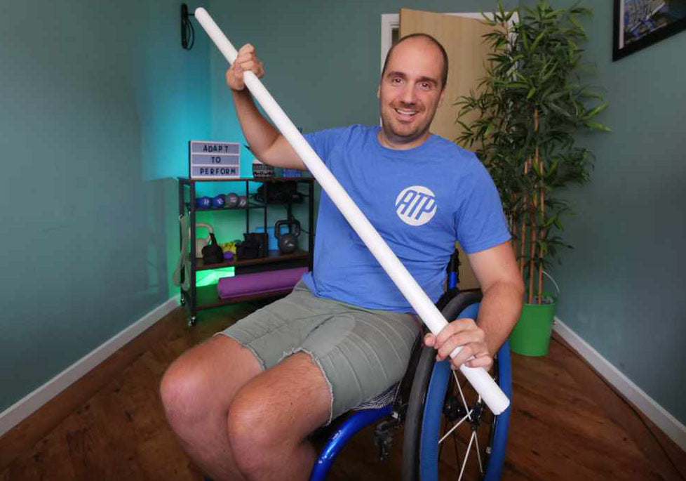 Ben Clark in his wheelchair holding a broom handle to demonstrate and adaptive fitness exercise.