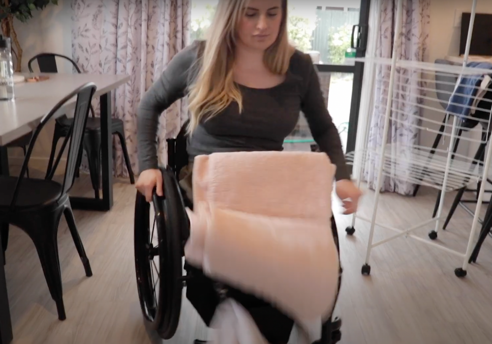 Girl in a manual wheelchair dropping towels from her lap without a LapStacker.
