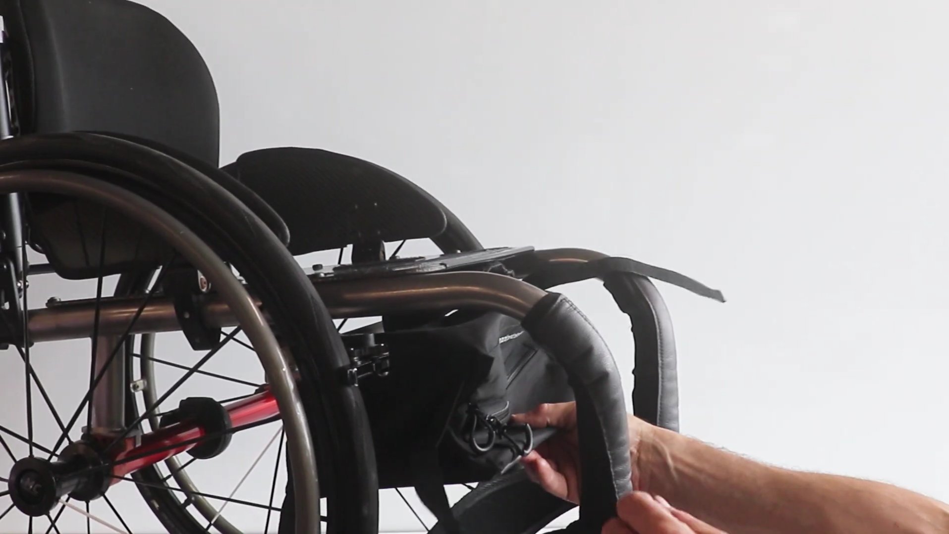 Close-up of a person installing an underseat wheelchair bag under a rigid frame wheelchair 