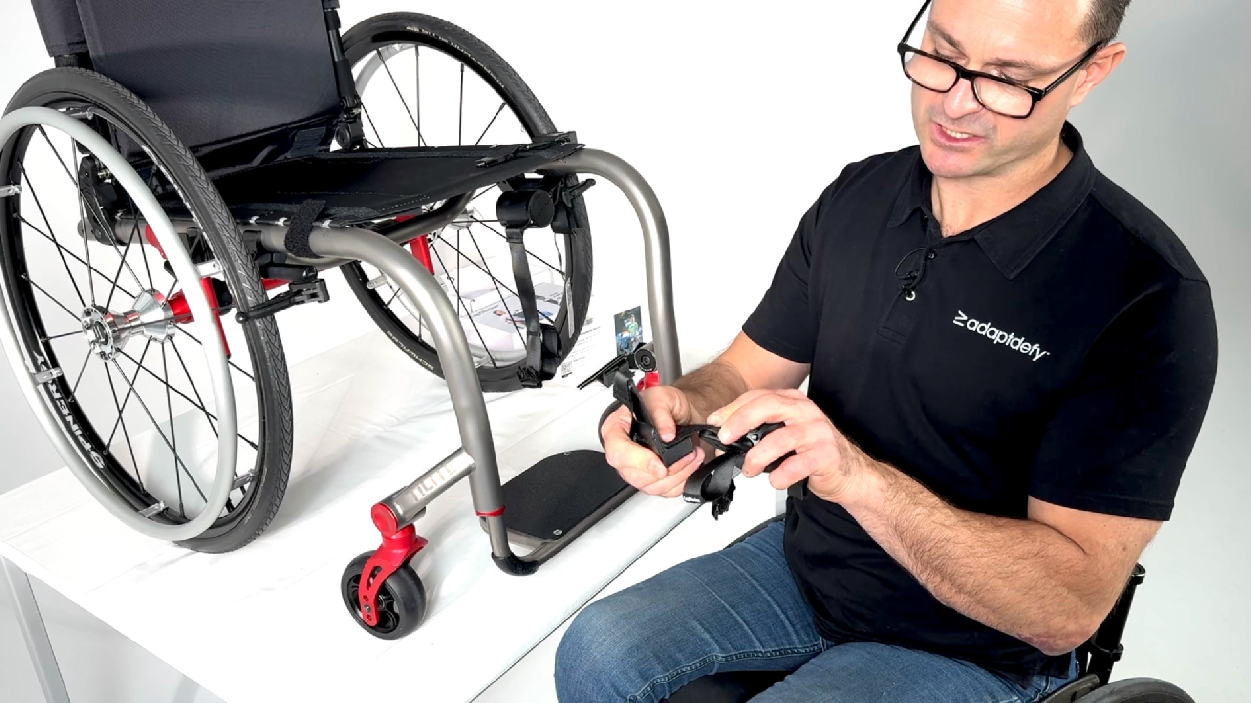 A man in a wheelchair explains and shows how to install a LapStacker Flex horizontally around the seat base of a manual rigid wheelchair.