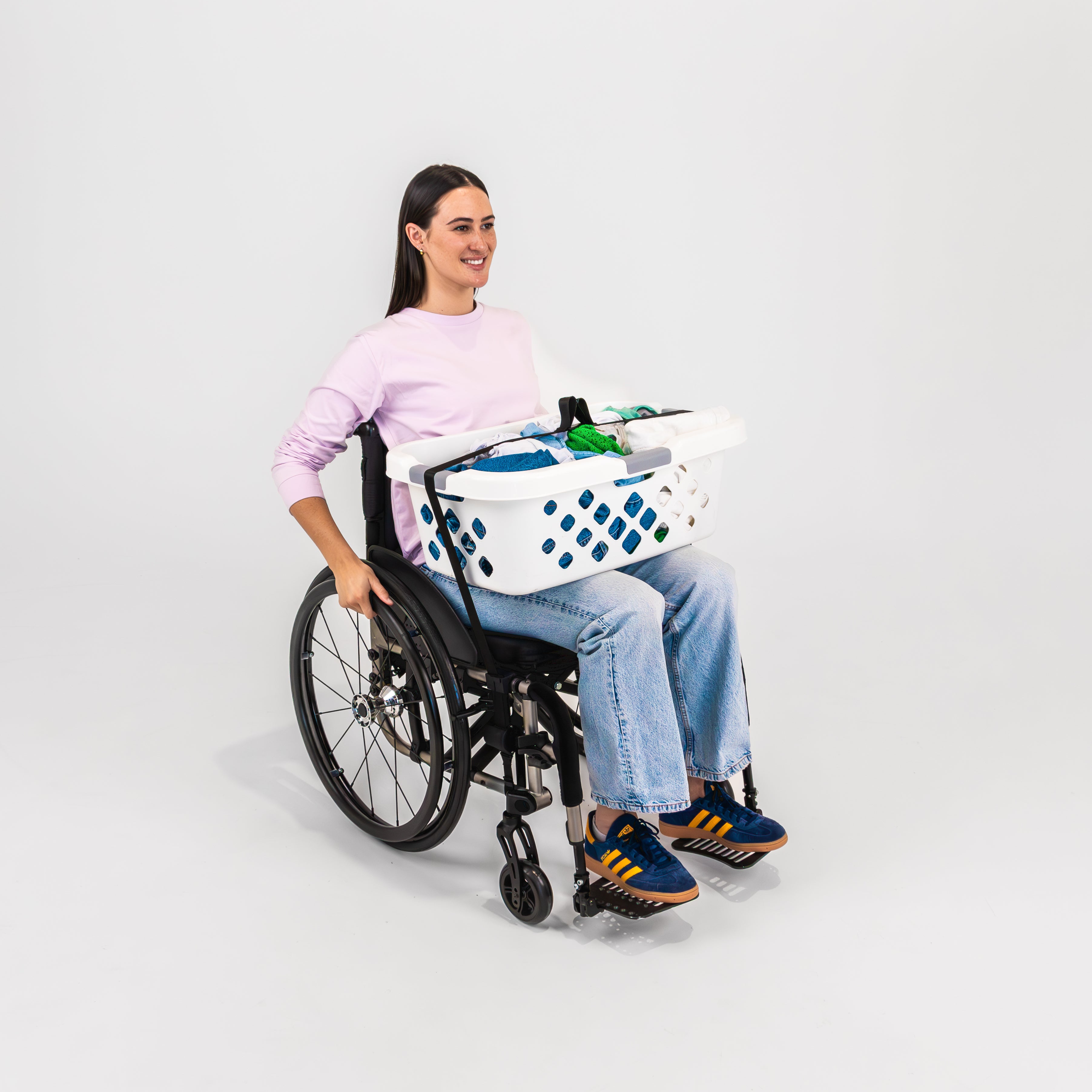 Smiling women with pink t-shirt seated in a wheelchair with a washing basket secured to her lap using LapStacker Flex.