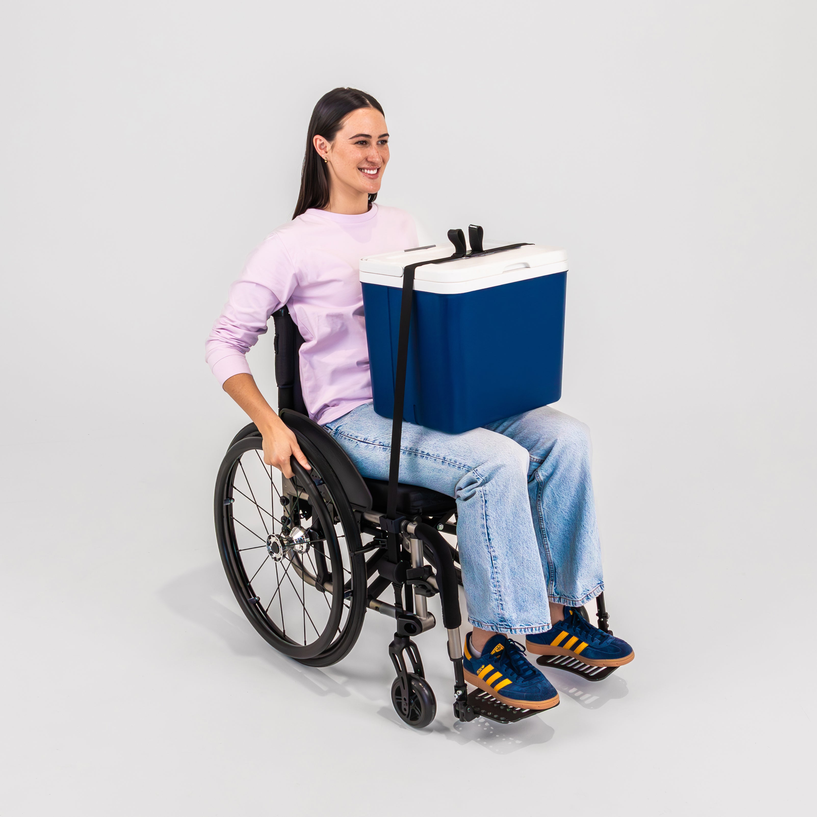 Smiling women seated in a folding wheelchair with a cooler or chilly bin secured to her lap using LapStacker Flex.