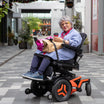 Silver haired woman in a Permobil power wheelchair with LapStacker securing shopping bags while she is smiling and holding a coffee
