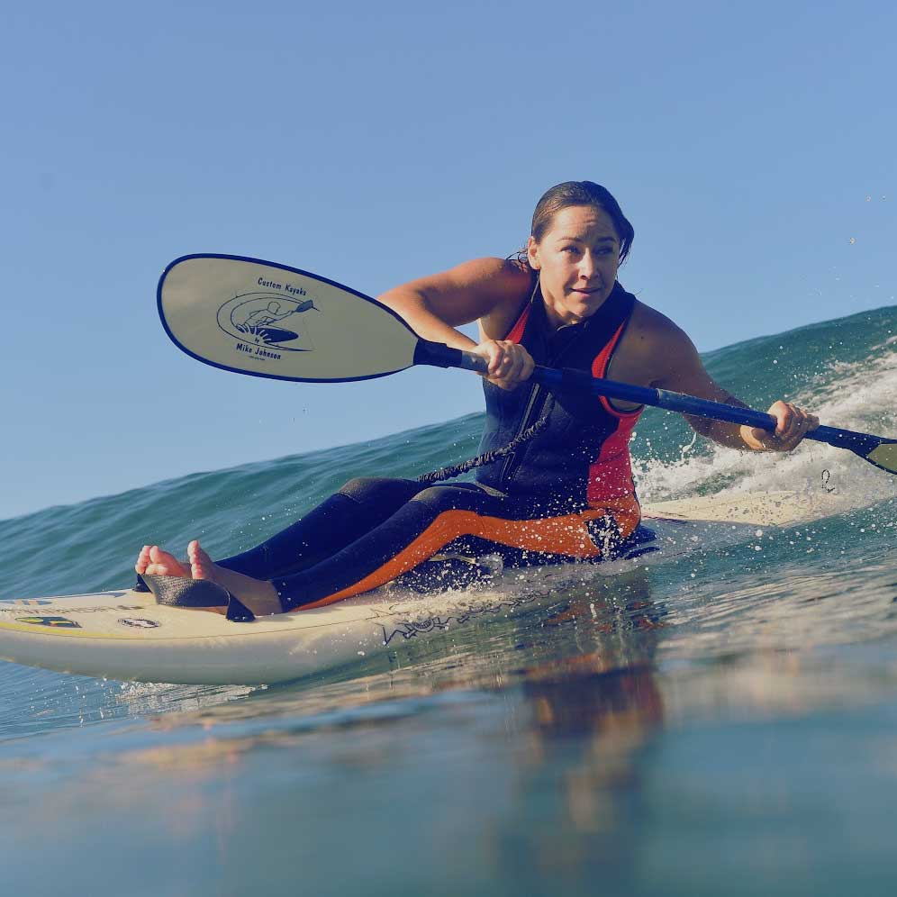 Alana Nichols adaptive surfing a wave on an adaptive wave ski, leaning forward and looking really excited