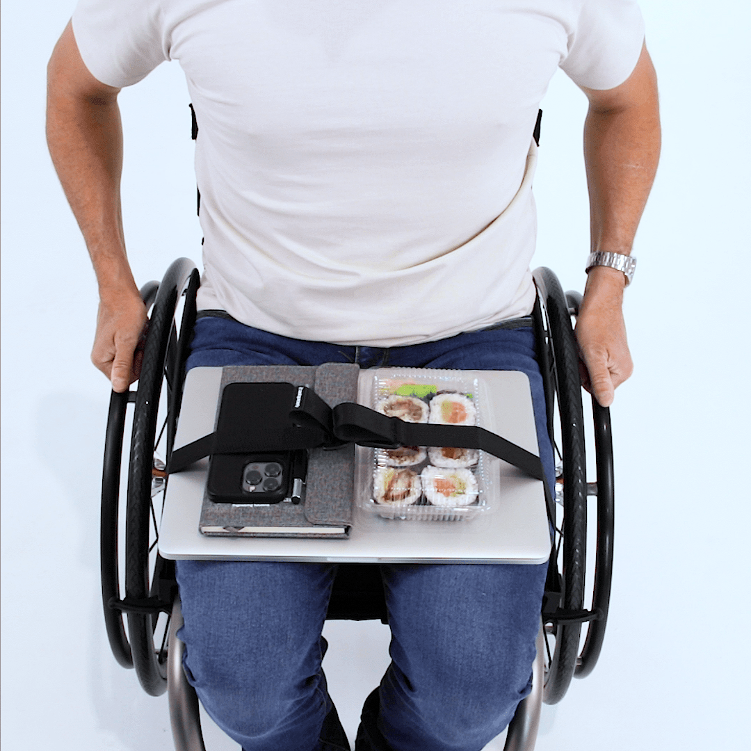 Overhead view of a man seated in a manual wheelchair  with a laptop, notebook, phone and packet of sushi secured with LapStacker Flex